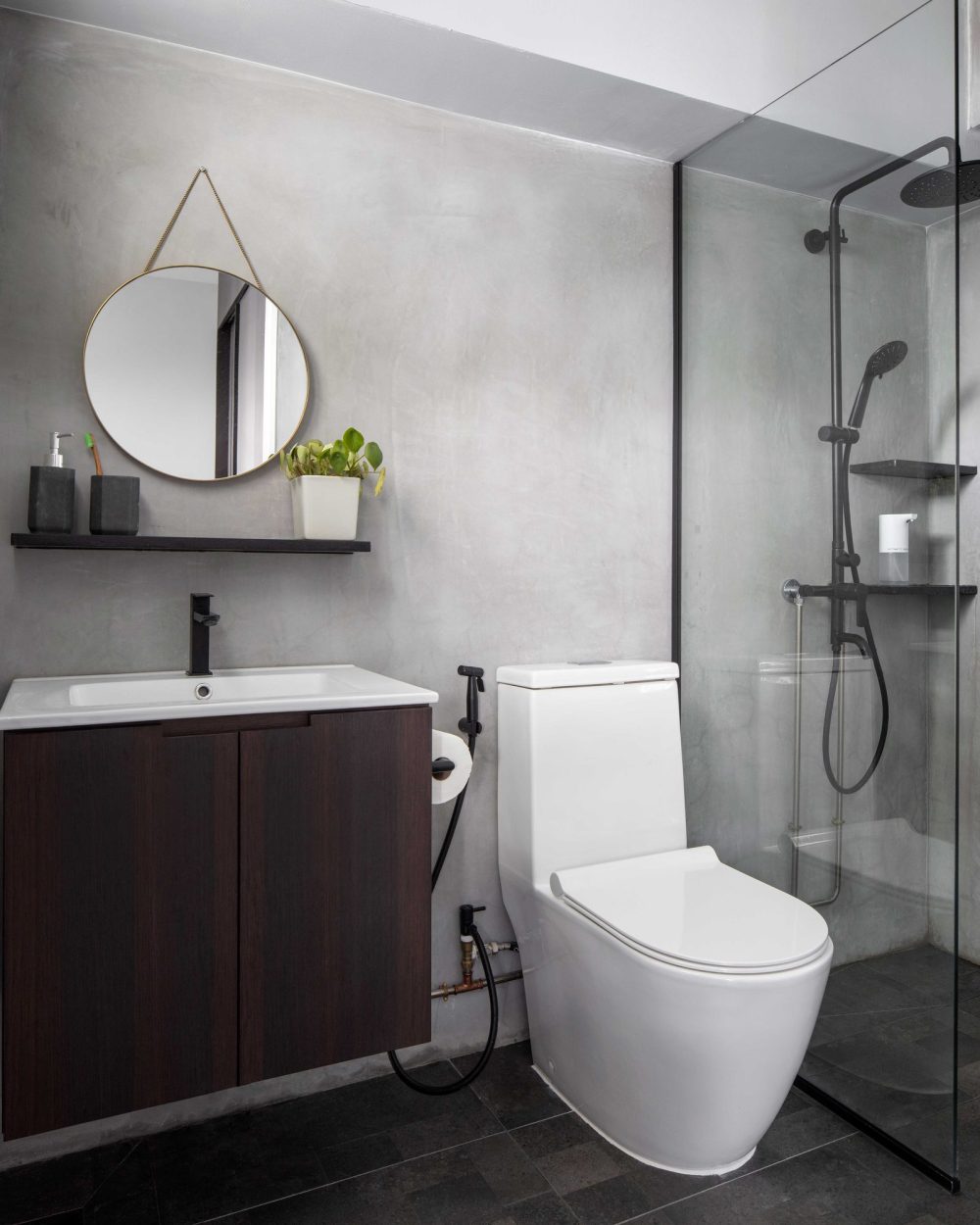 Raw concrete plaster continues into the bathroom, paired with a round hanging mirror, dark timber vanity and a black-fitted rain shower.