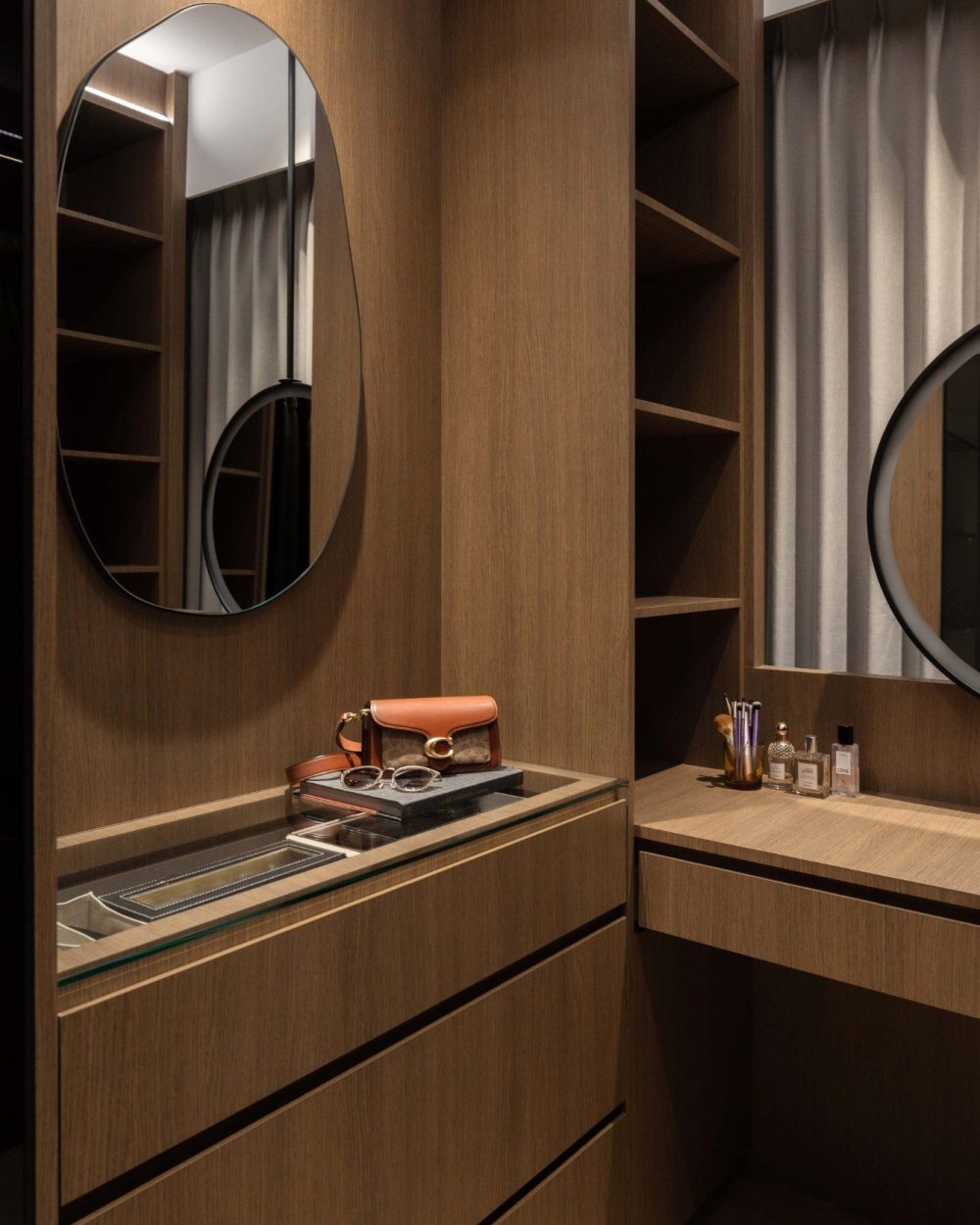 The dressing table pairs an oval mirror with a glass-topped drawer for jewellery and everyday essentials, with open shelving to the side for bags and