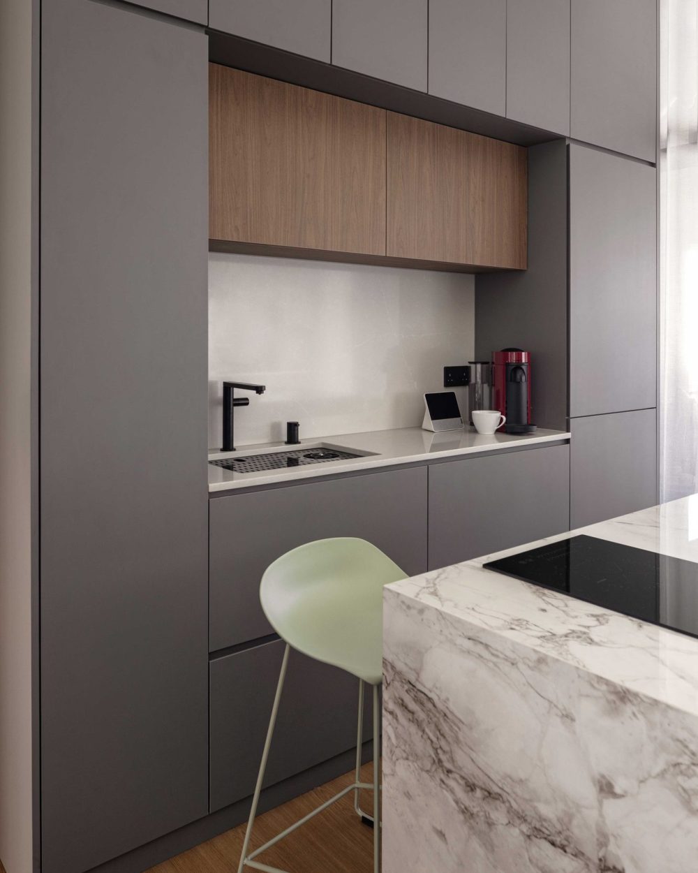 Open counter space and a sage green stool make this corner of the kitchen a flexible spot for quick meals or homework.