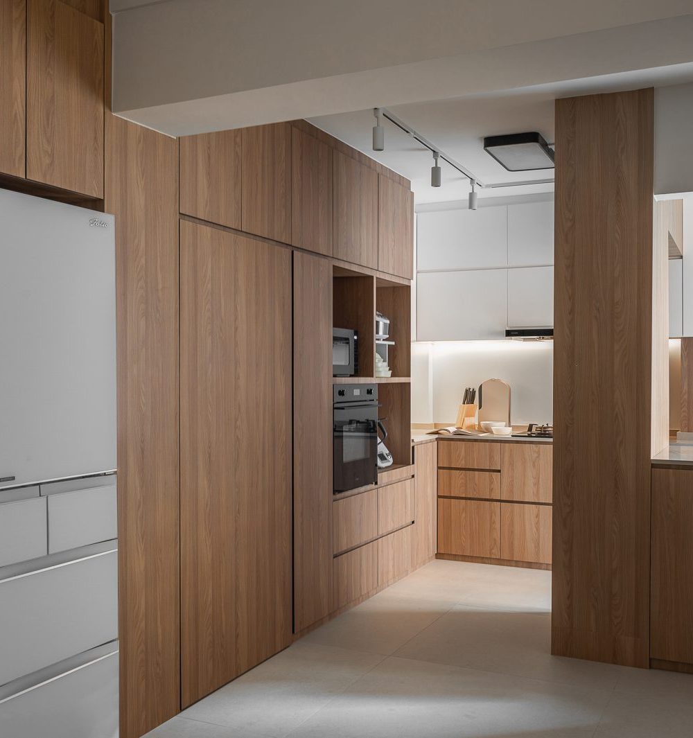 A white refrigerator and full-height timber storage line the corridor between the two kitchen zones, keeping everything within reach.