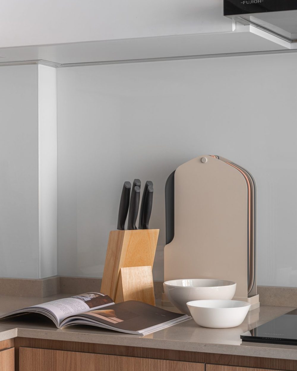 A wooden knife block and stacked bowls sit ready at the counter's edge, framed by a glass splashback panel.
