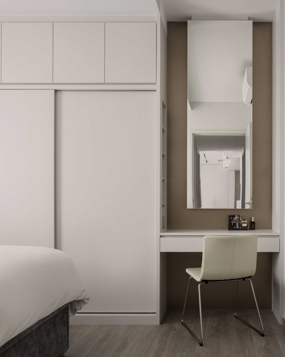 Soft taupe walls and warm cove lighting frame the dressing nook, styled simply with skincare essentials.