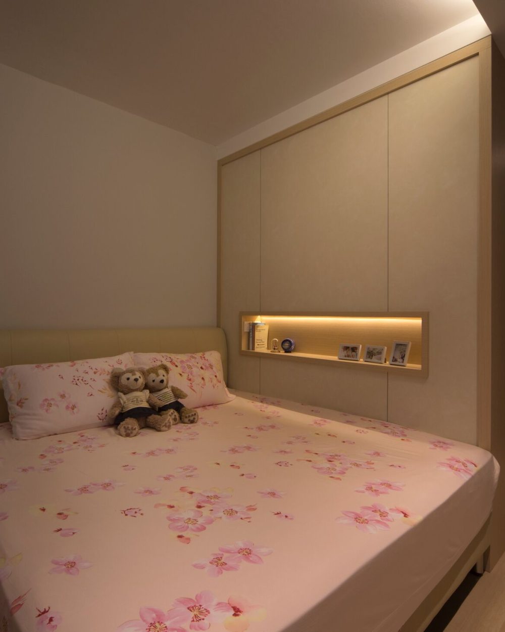 A backlit shelf built into the headboard wall keeps books and keepsakes close at hand, framed by soft taupe leather upholstery.
