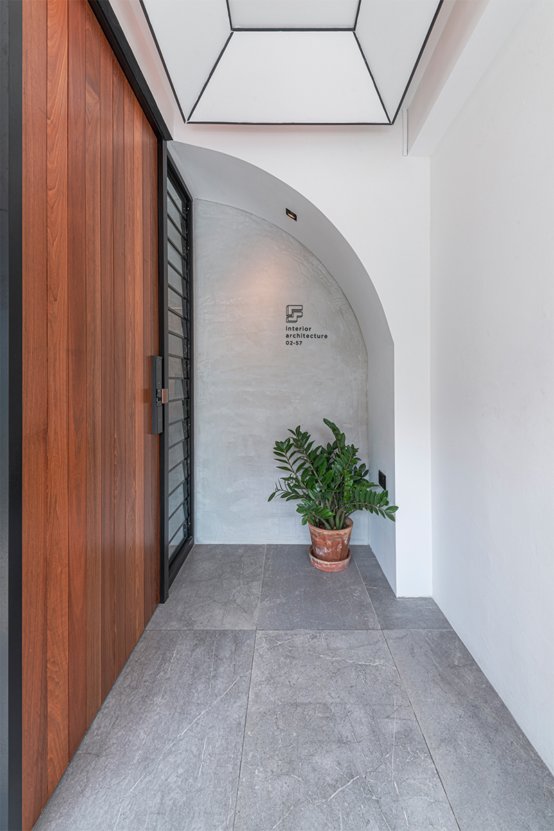 A plastered archway frames the reception niche, finished with a solid timber door and a simple potted plant.
