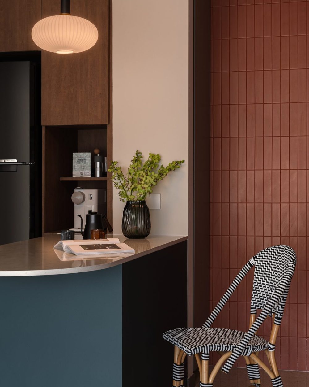A curved stone counter and pendant light sit against the terracotta tile wall, paired with a black-and-white woven bistro chair.