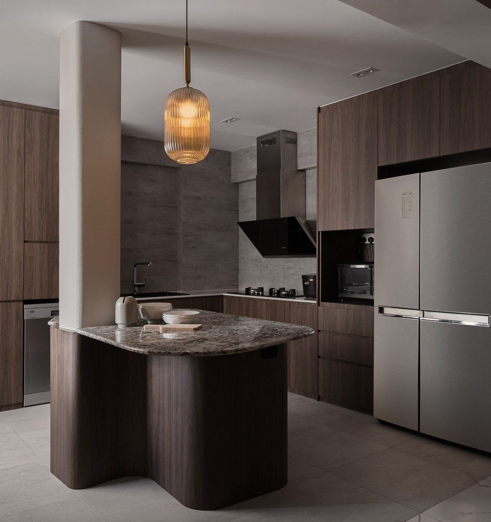 A curved marble-topped island anchors the kitchen beneath a ribbed glass pendant light, framed by dark timber cabinetry, a built-in hood and a full-he