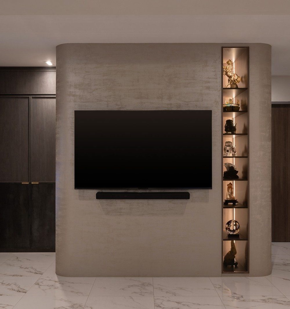 A curved plaster-finished TV wall houses a lit display niche of collectibles, framing the transition between the living area and the bedroom corridor.
