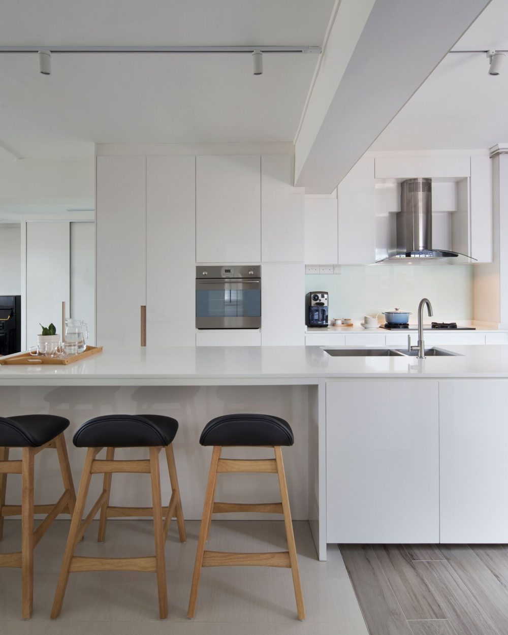 A curved stainless steel range hood and glass splashback anchor the kitchen, finished with white cabinetry and warm timber handle strips.