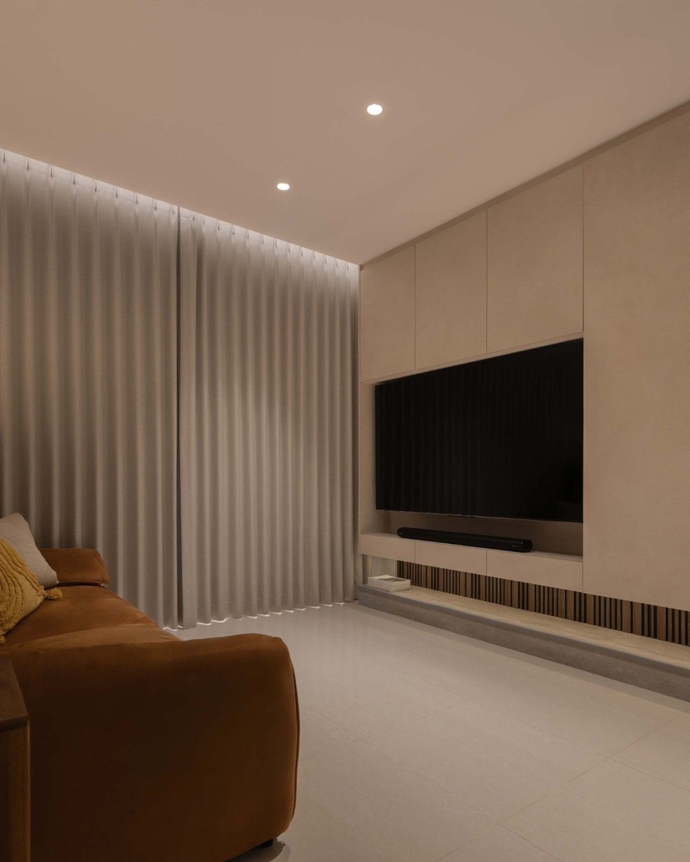 The living room's TV feature wall curves gently into the room, finished in a soft plaster tone with a striped timber and stone plinth below.