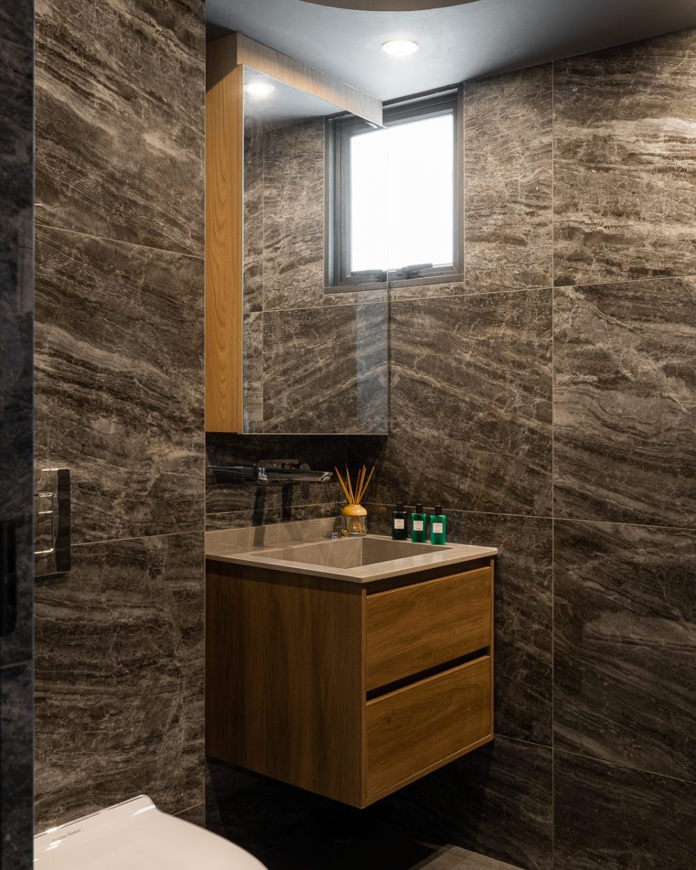 Deep grey stone tiling gives the second bathroom a moodier, more dramatic finish, paired with a warm oak floating vanity.