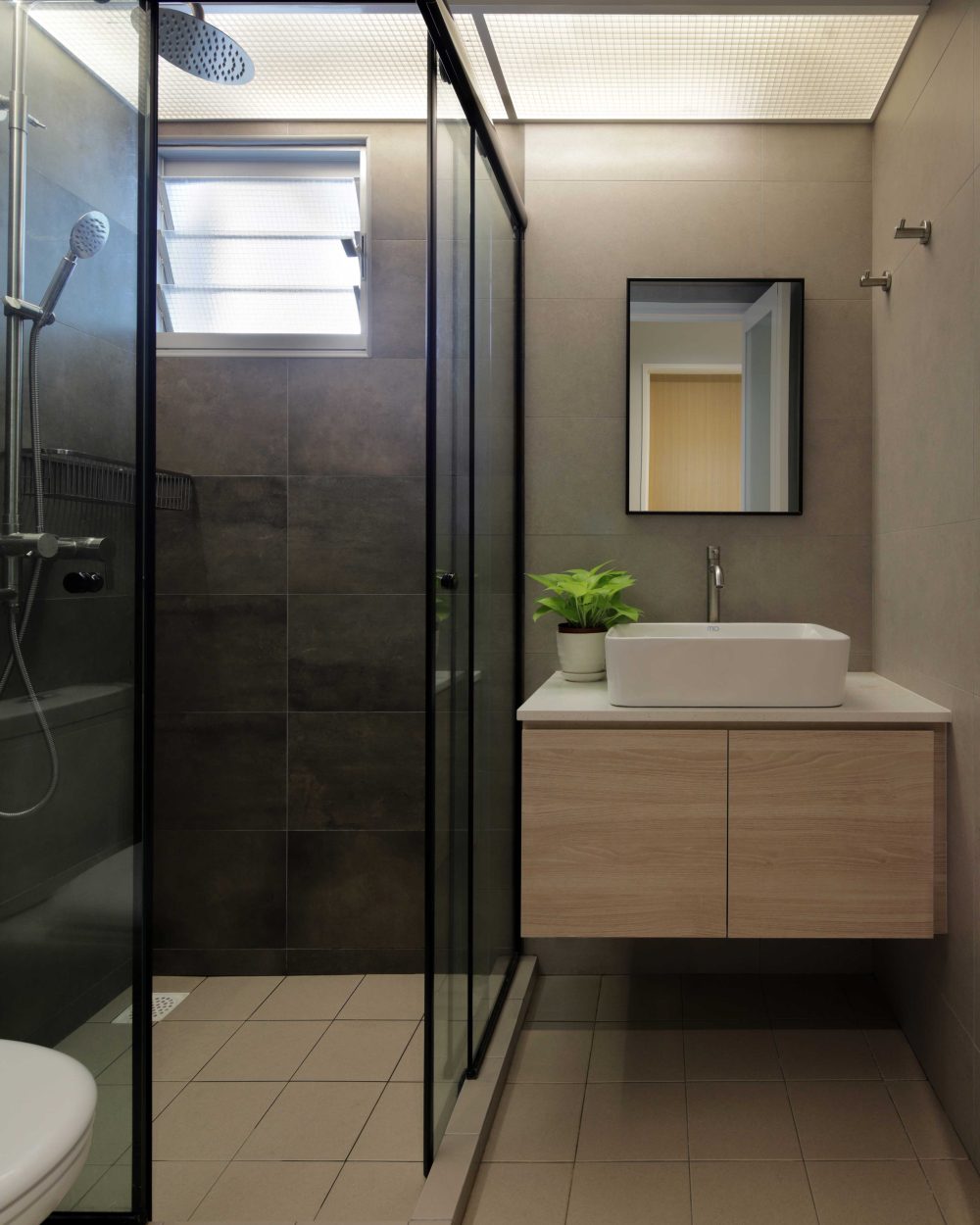 Charcoal-toned tiles line a glass-enclosed shower, paired with a floating timber vanity and vessel sink in the ensuite bathroom.