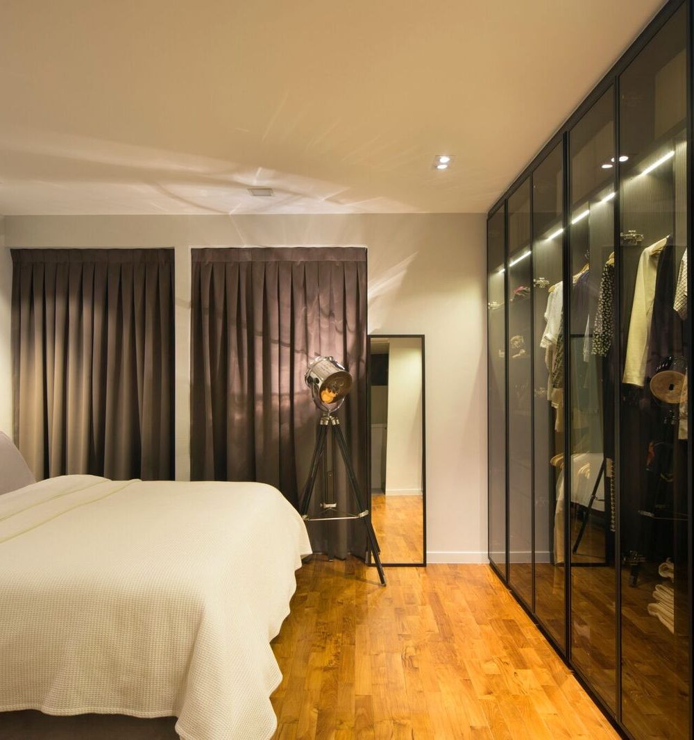 A button-tufted black headboard anchors the bedroom, set against brown curtains and a full glass-fronted wardrobe wall.