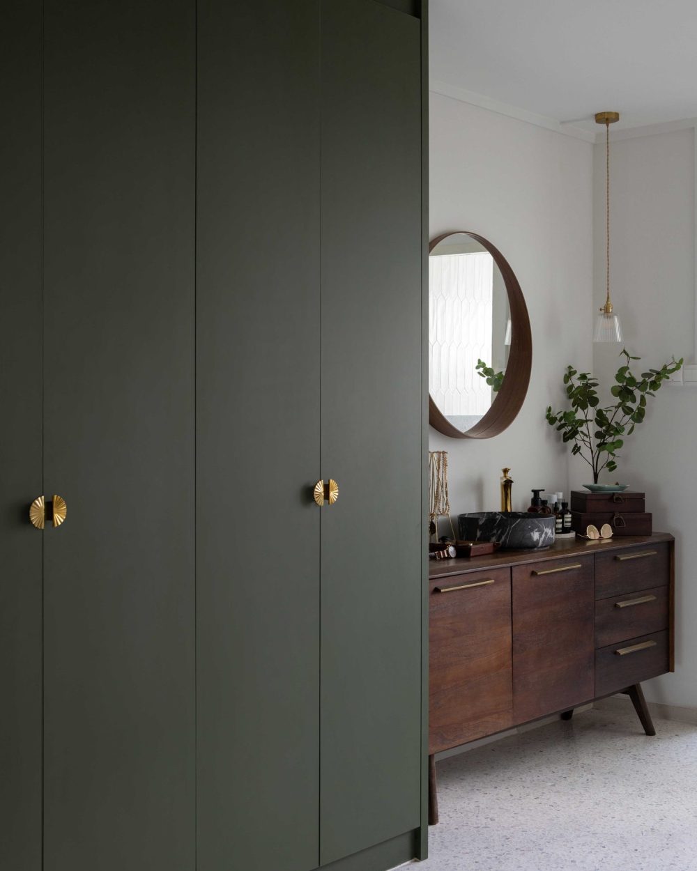 Forest green wardrobes with brass pull handles open onto a walnut vanity and round mirror in this dressing corner.