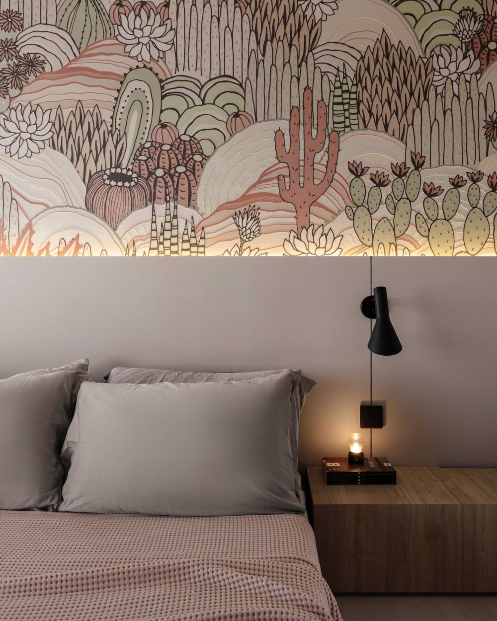 An illustrated desert mural wraps the headboard wall, paired with soft pink and grey bedding and a sculptural black wall sconce.