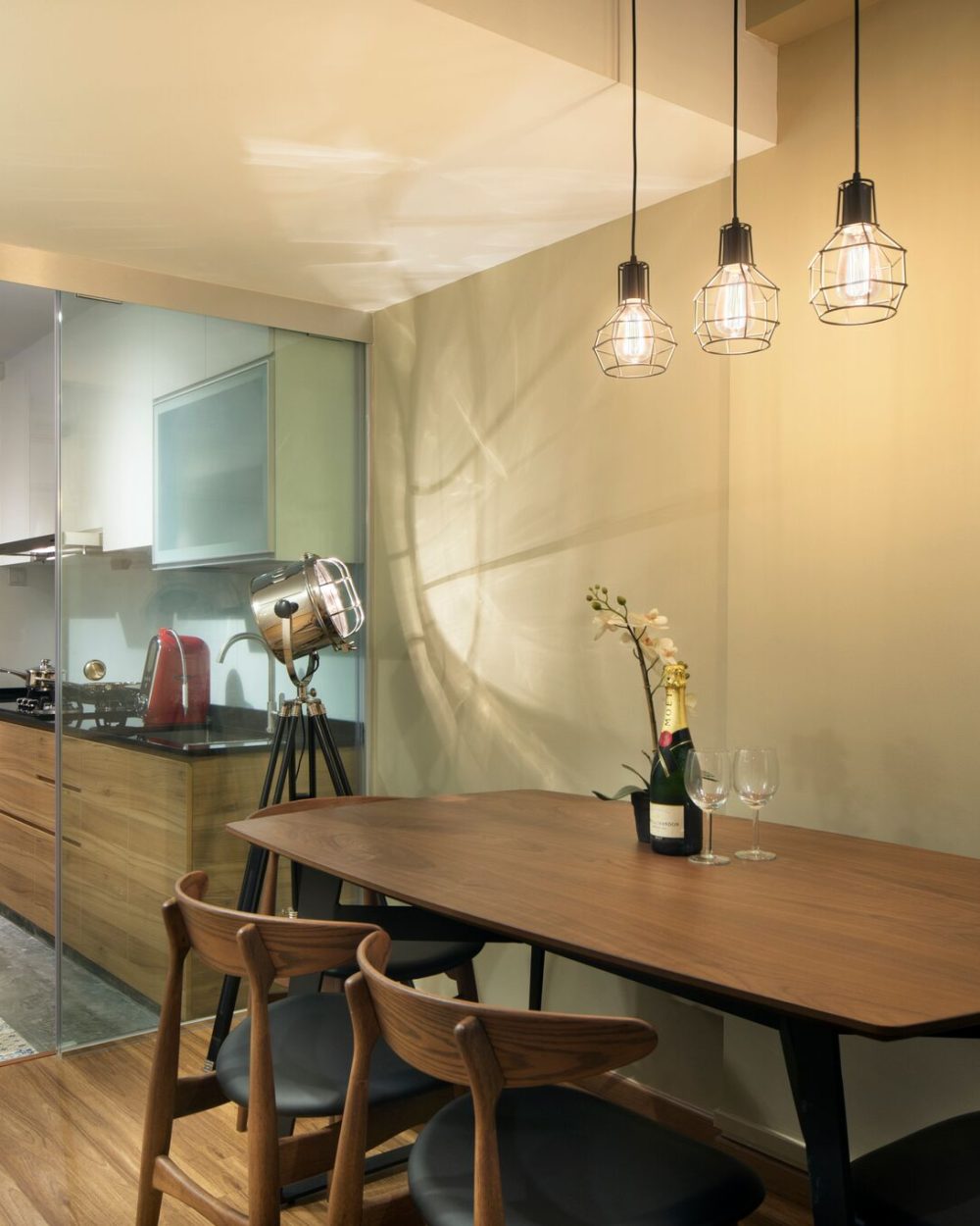 Three wire cage pendant lights hang over an oval walnut dining table, with a glass sliding door opening onto a patterned-tile kitchen floor.