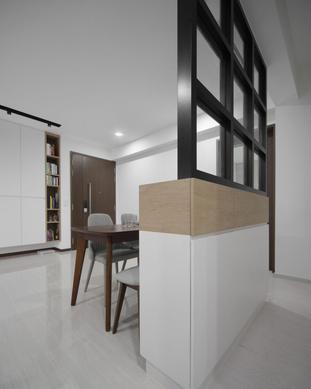 The same glass partition frames a wood-and-white cabinet in the dining nook, with an open bookshelf built into the adjoining wall.