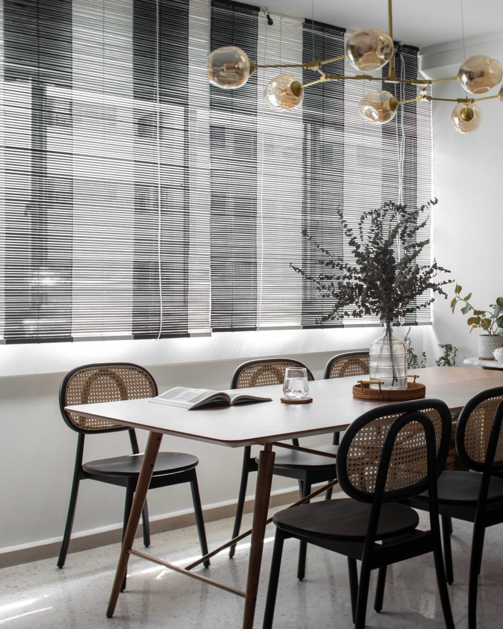 A brass multi-arm chandelier with amber glass globes hangs over a walnut dining table, surrounded by black cane-back chairs.