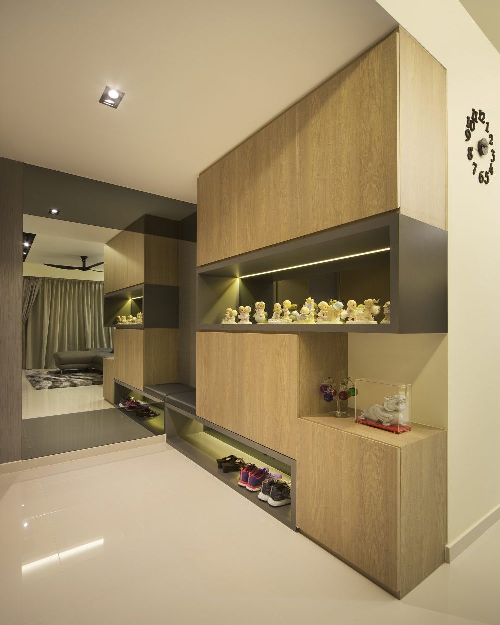 Timber-and-grey shoe cabinetry opens into a backlit display niche for collectibles, with a full mirror extending the entry visually.