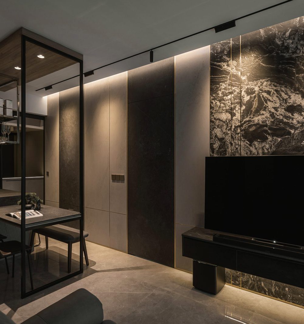 A richly veined black marble panel with brass inlay lines rises behind the TV, framed by sheer curtains and soft cove lighting.