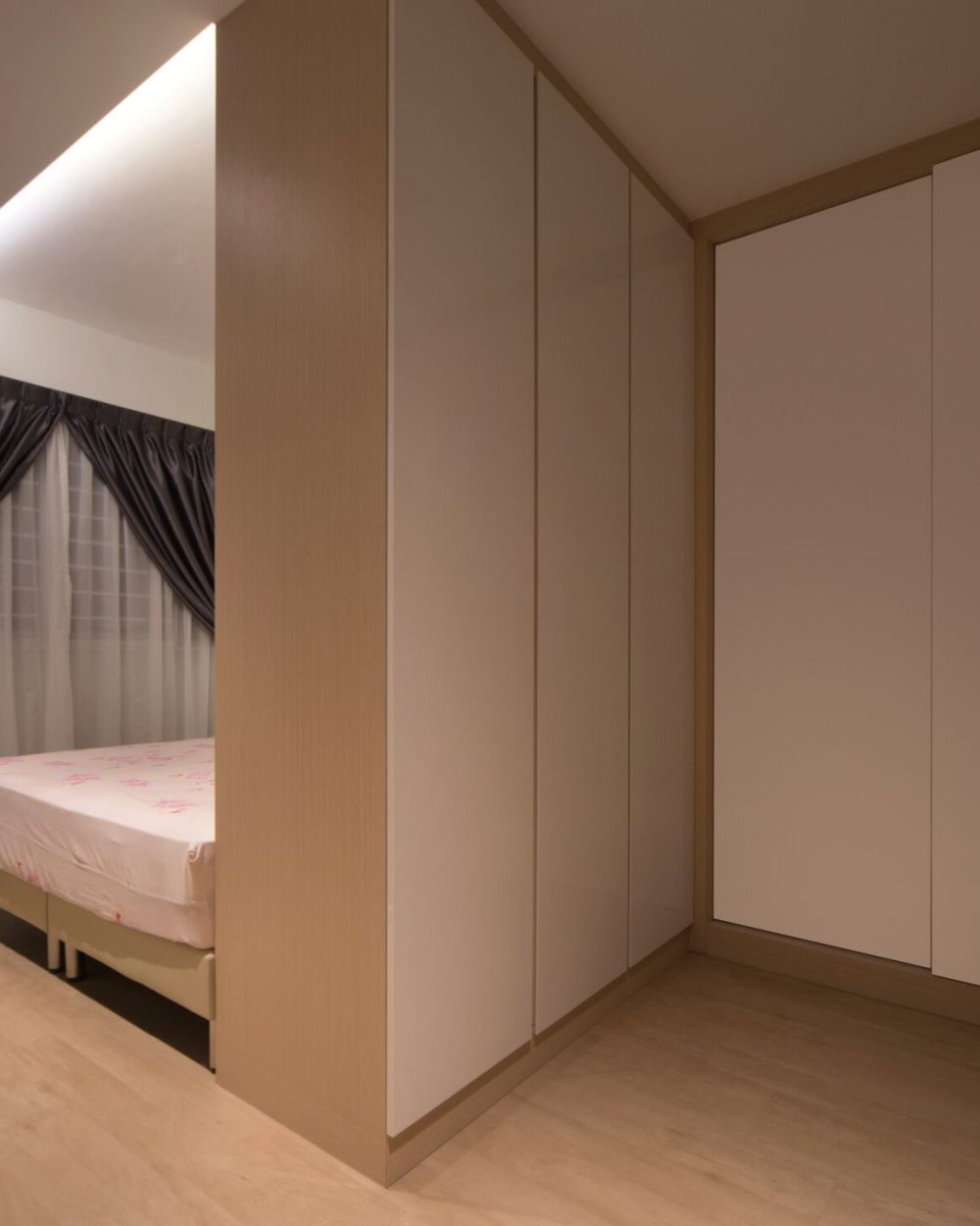 Floor-to-ceiling grey drapery softens the bedroom's window wall, opening into a glossy white wardrobe corner beyond.