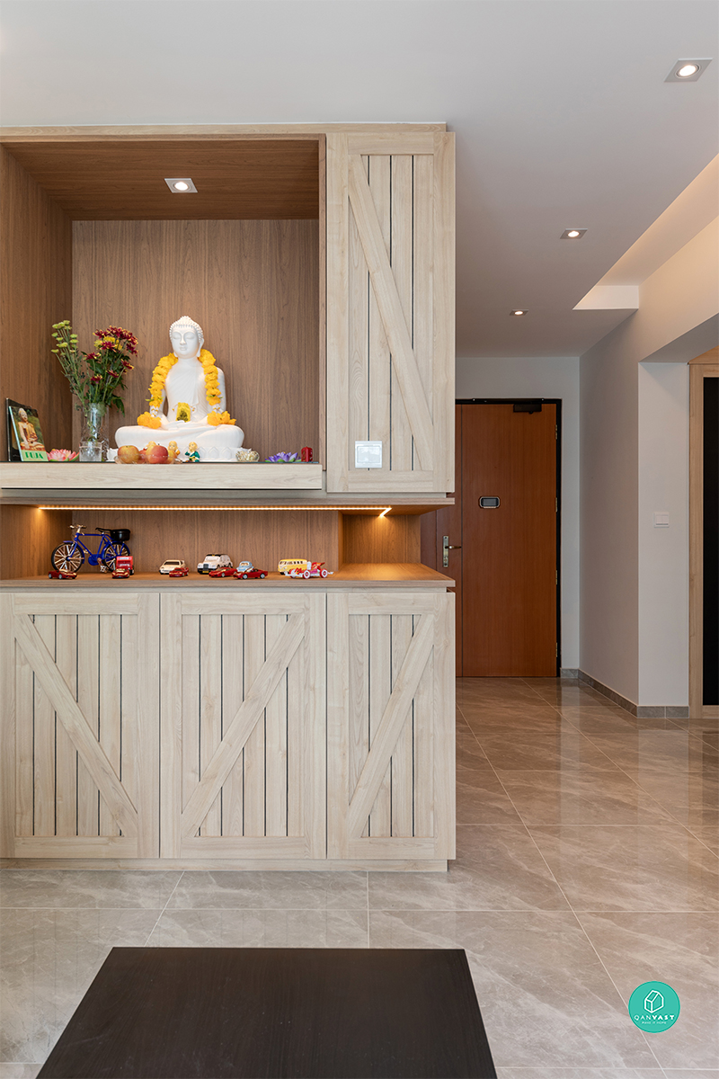 A dedicated altar nook sits within the entryway carpentry, framed by the same timber slats and lit by a warm recessed spotlight.