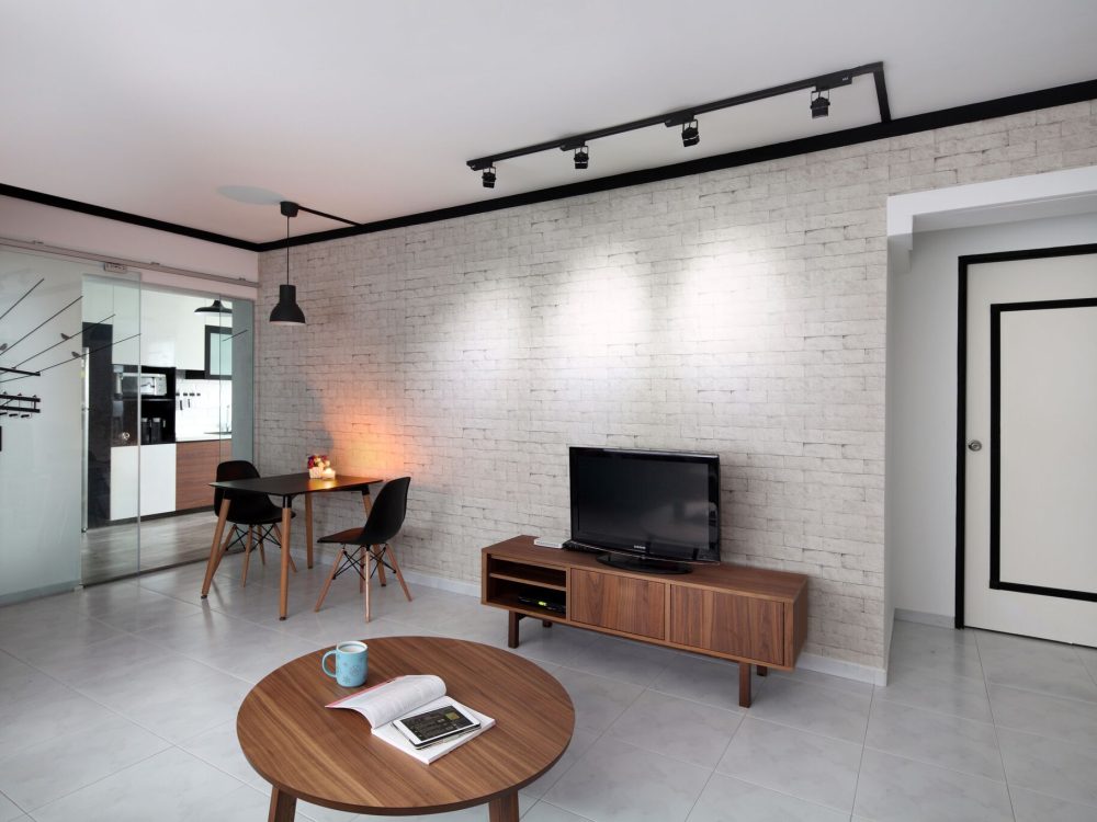A raw-textured brick-effect wall anchors the living and dining space, framed by black track lighting and a slim walnut TV console. A glass-panelled sl