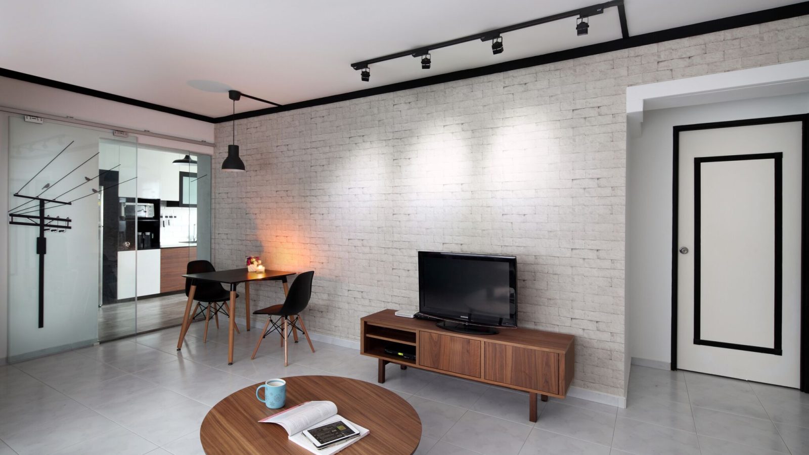 A raw-textured brick-effect wall anchors the living and dining space, framed by black track lighting and a slim walnut TV console. A glass-panelled sl