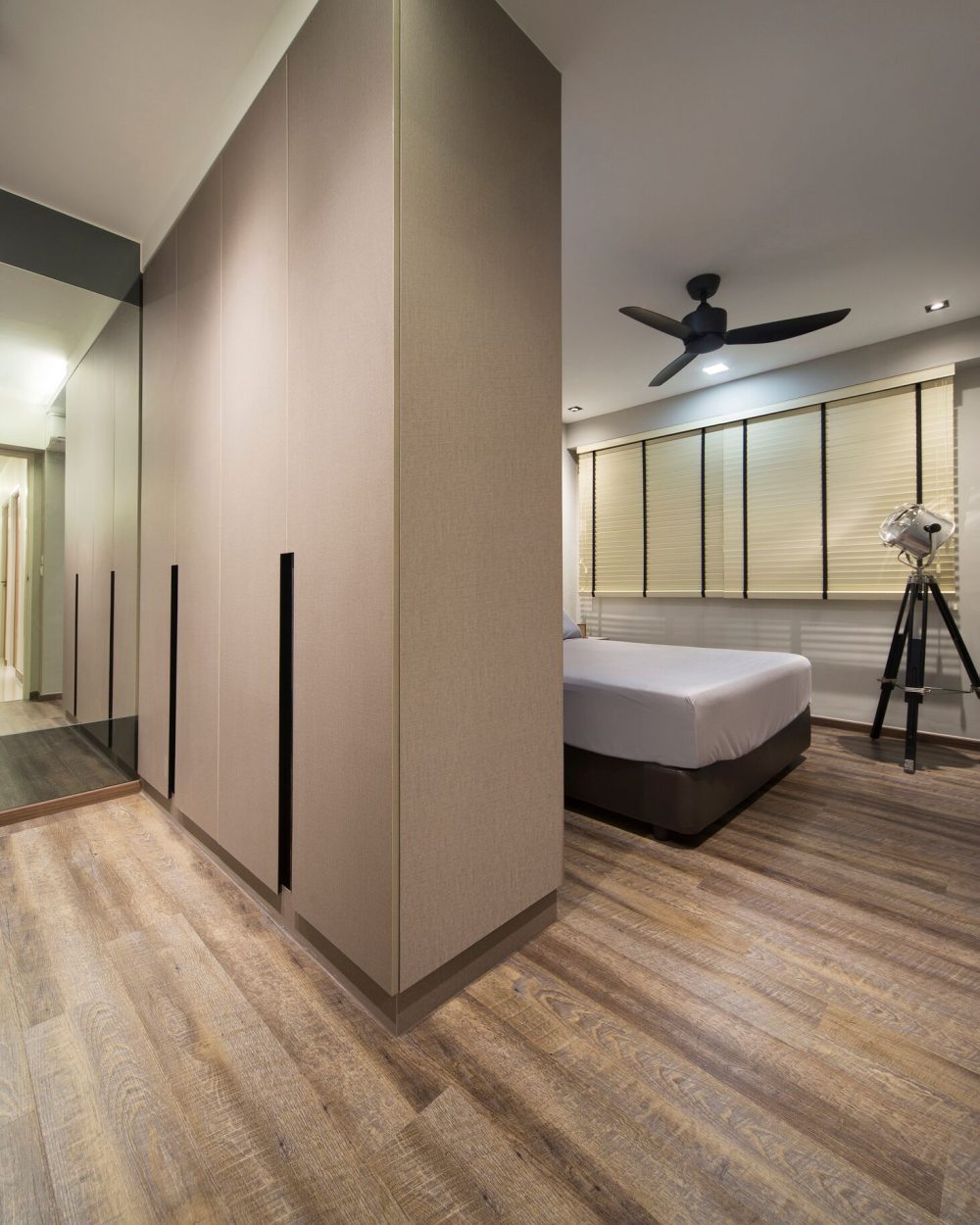 Fabric-textured wardrobe panels with recessed black pulls line the hallway leading into the bedroom, mirrored on the opposite wall to widen the space