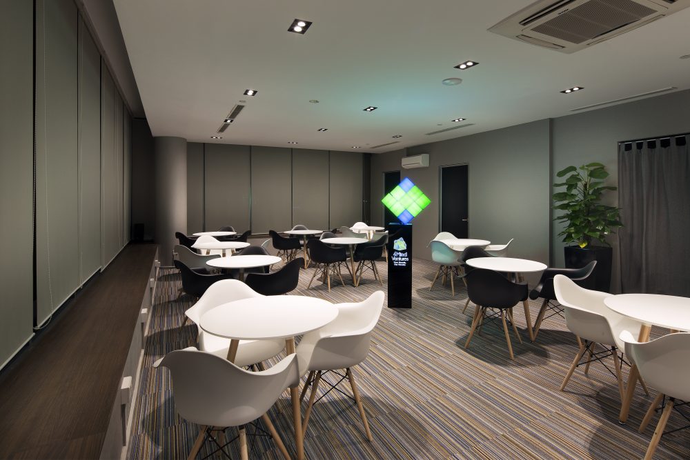 Round white tables and Eames-style chairs furnish a multi-purpose training room, lit by a floor-standing branded light box.