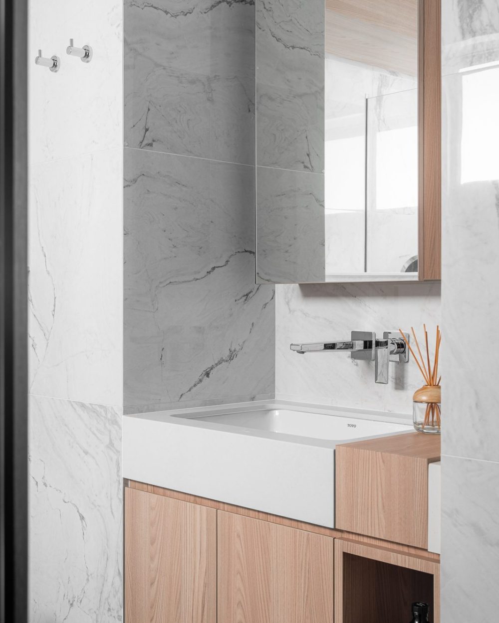 A rectangular floating sink and mirrored cabinet sit beneath a marble-tiled wall, lit by a frosted window.