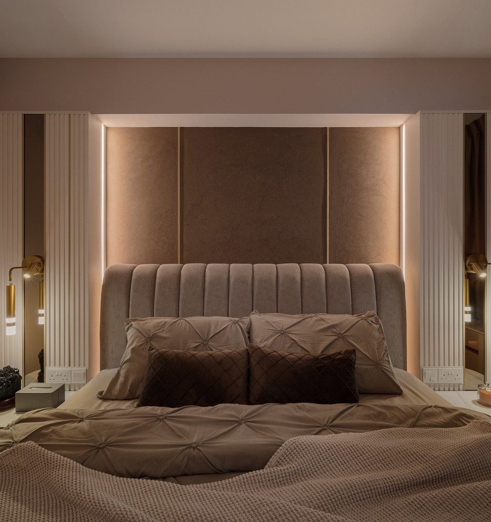 A channel-tufted headboard is framed by fluted wardrobe panels and mirror strips on either side, with brass reading lights and warm cove lighting buil