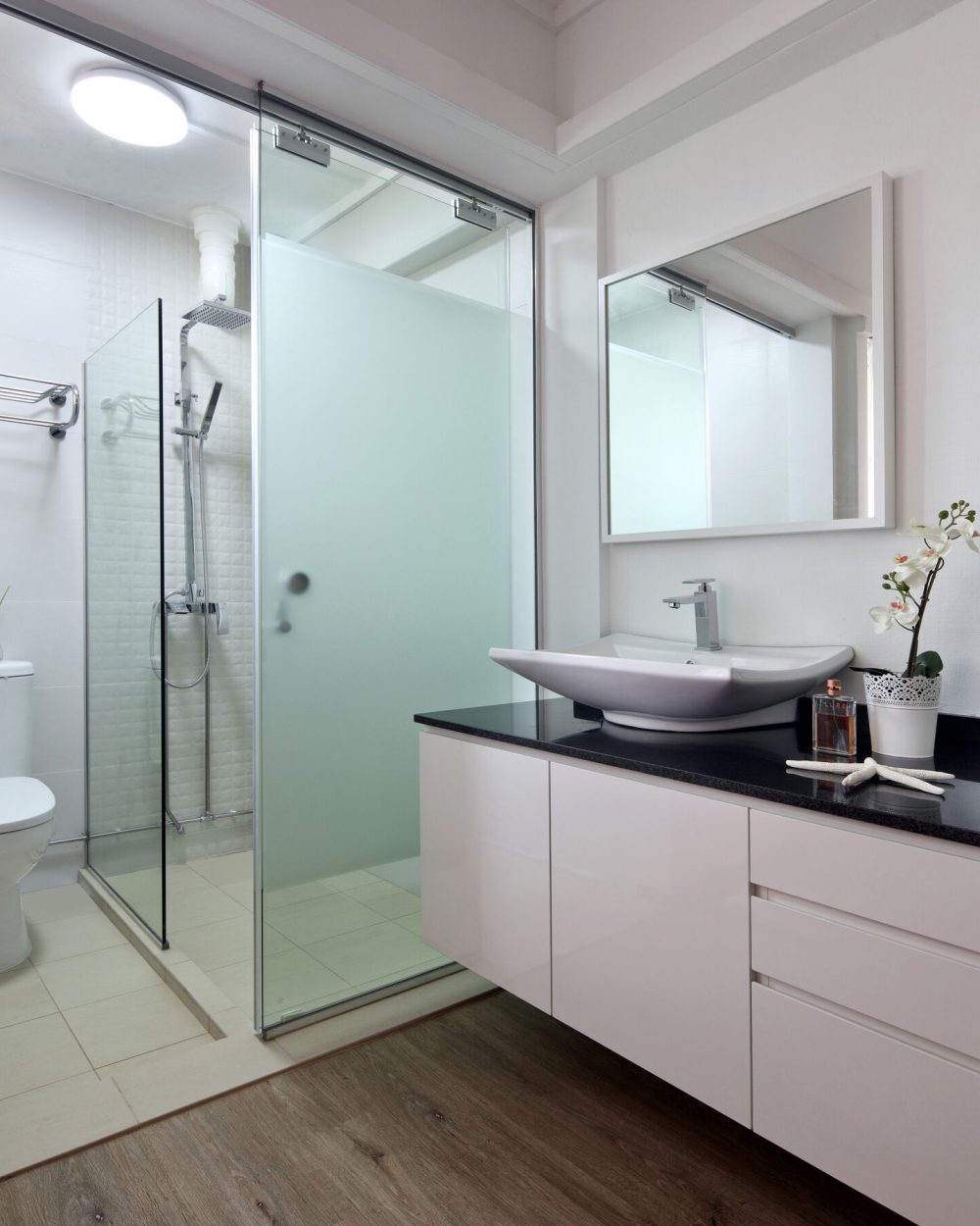 A frameless glass shower and floating white vanity with a black stone counter give the ensuite a clean, hotel-like finish.