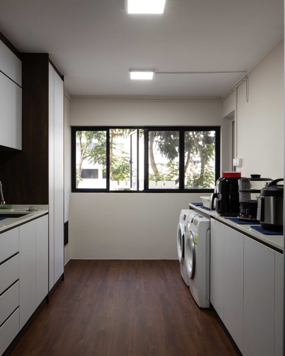 A long galley layout houses the washing machine, rice cooker and everyday kitchen appliances, lit by a garden-facing window.