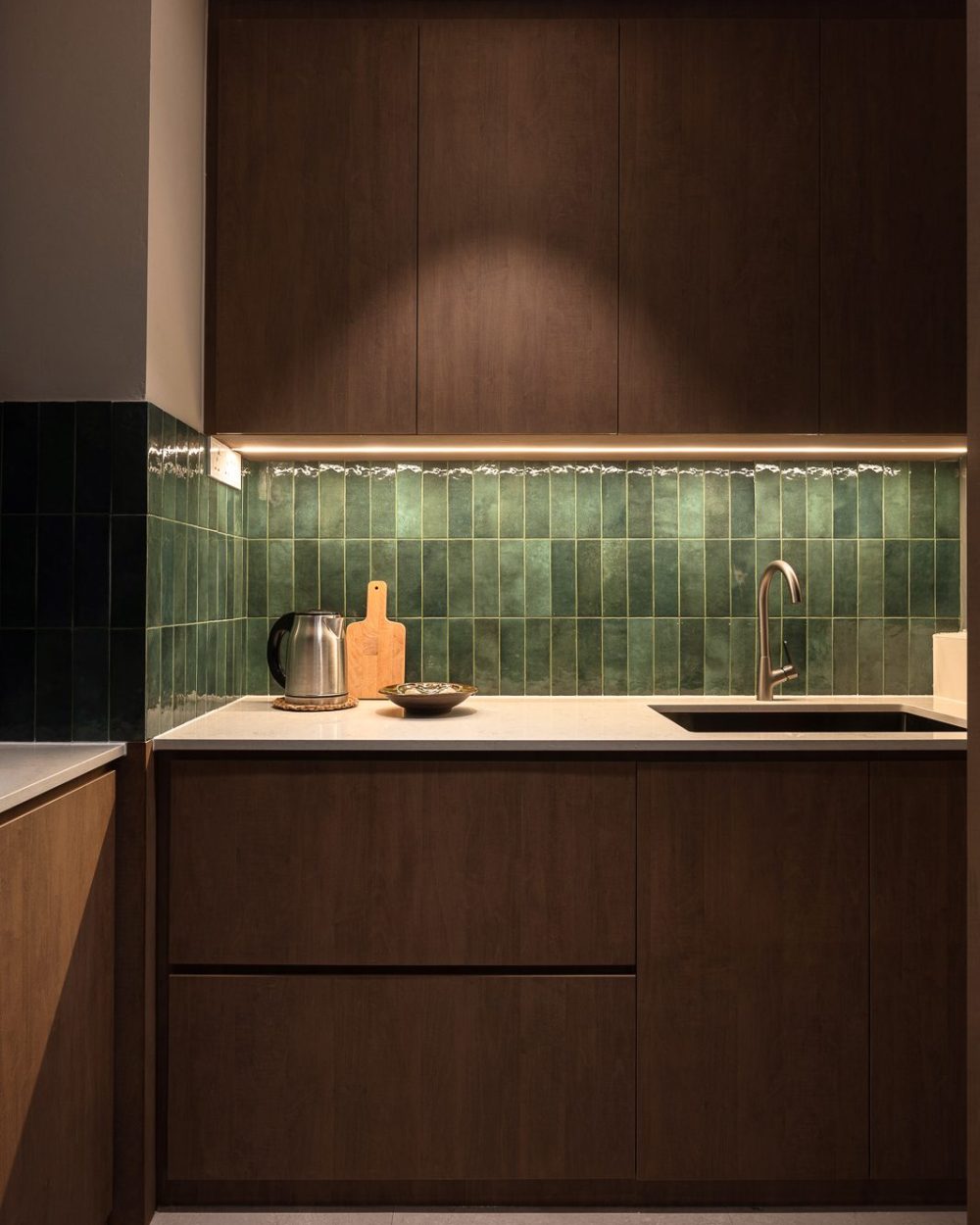 A gas hob and built-in oven and microwave column complete the wet kitchen, continuing the green tile and dark timber palette.