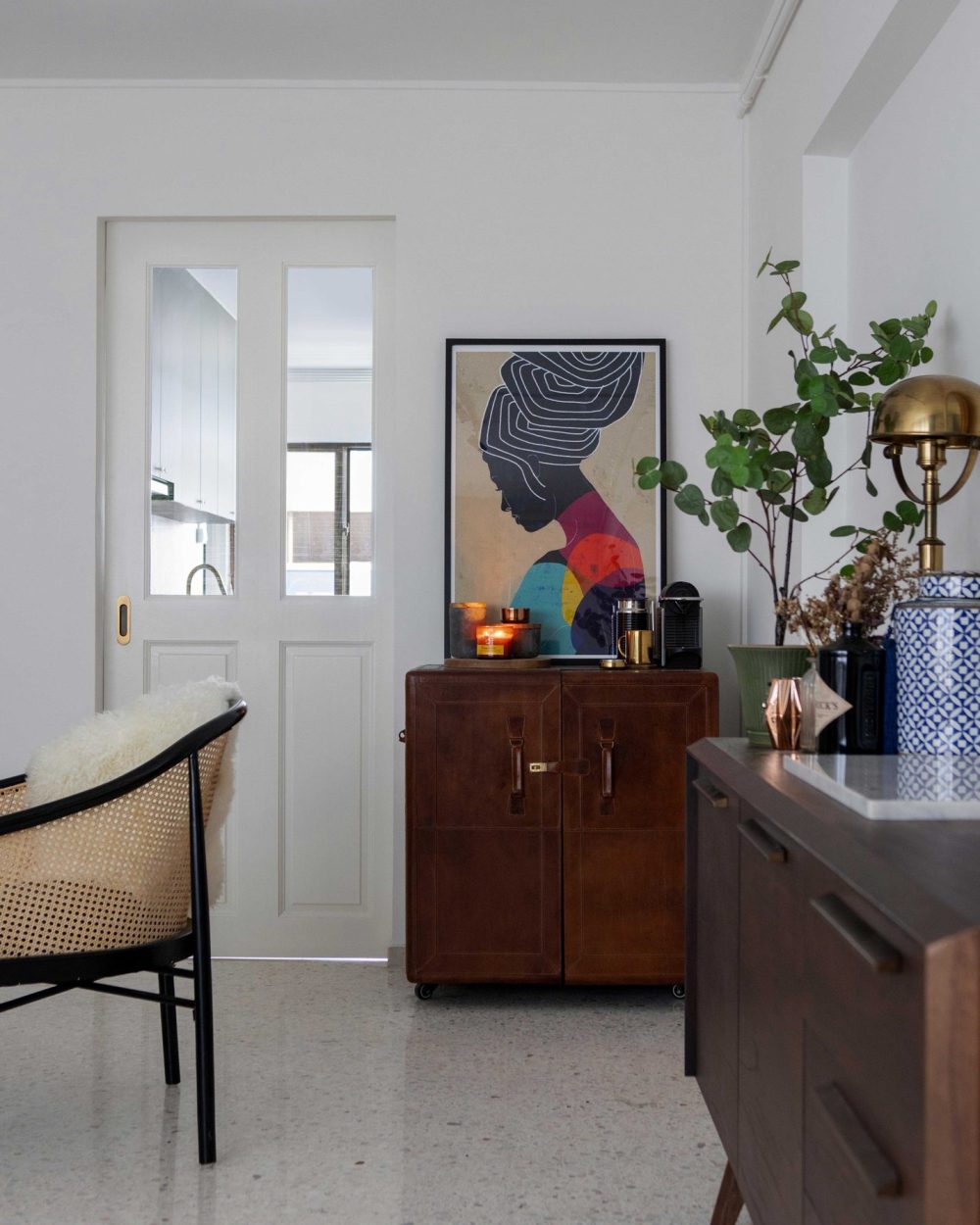 A bold graphic art print and a vintage leather trunk cabinet greet visitors at the entrance, paired with a cane-and-sheepskin chair.