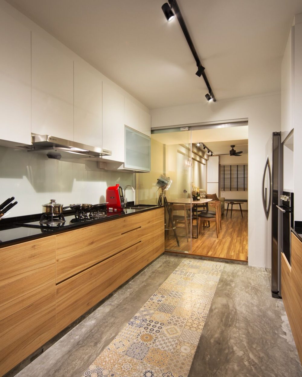 White gloss upper cabinets meet warm wood-toned lower units and a black stone countertop, with a strip of patterned floor tiles running the length of