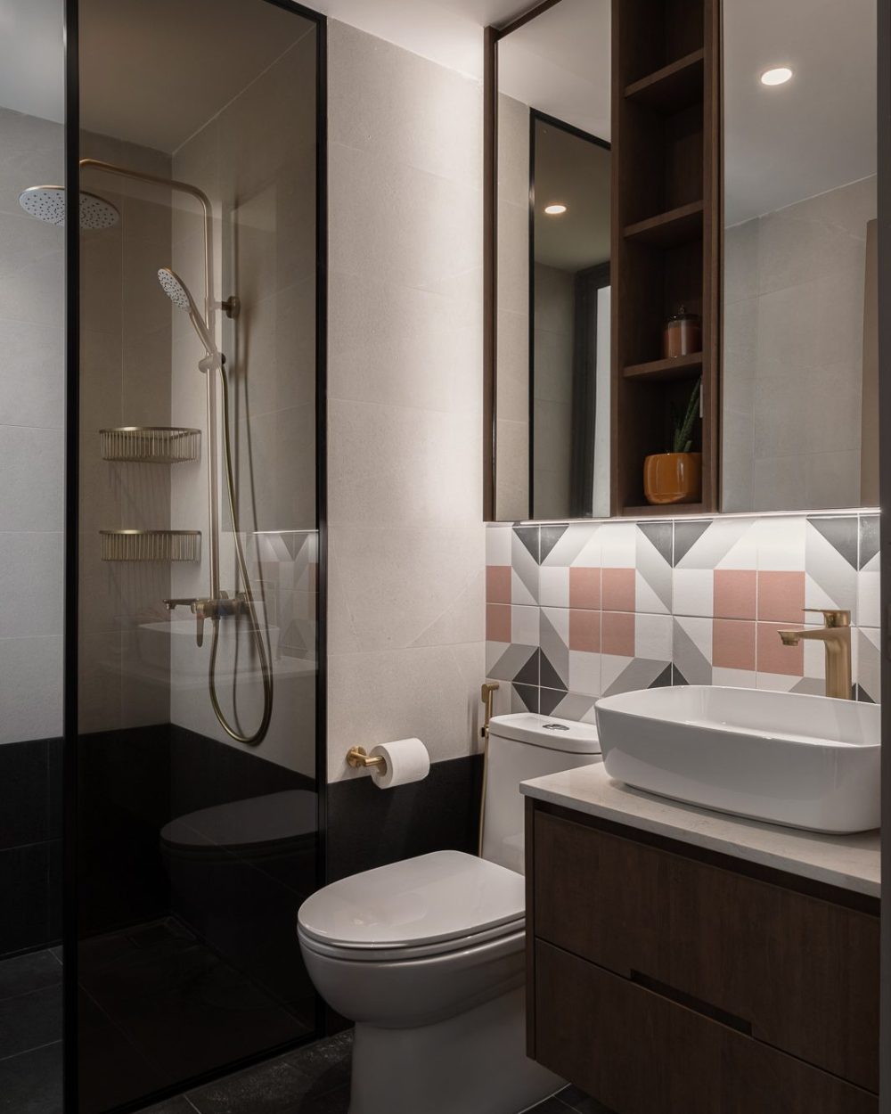 A pink, grey and white geometric tile backsplash pairs with brushed gold fixtures and a glass-enclosed shower for a playful, elevated ensuite.