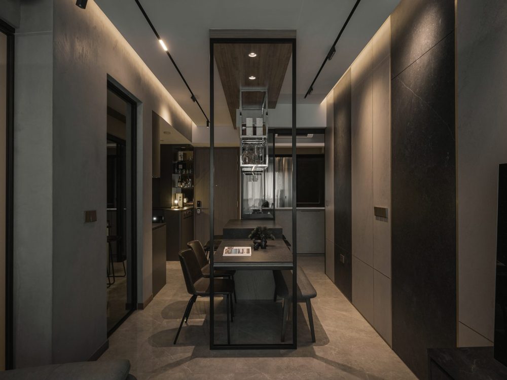 A suspended glass-and-steel wine rack anchors the dining area, framed by dark stone-clad walls and warm cove lighting.