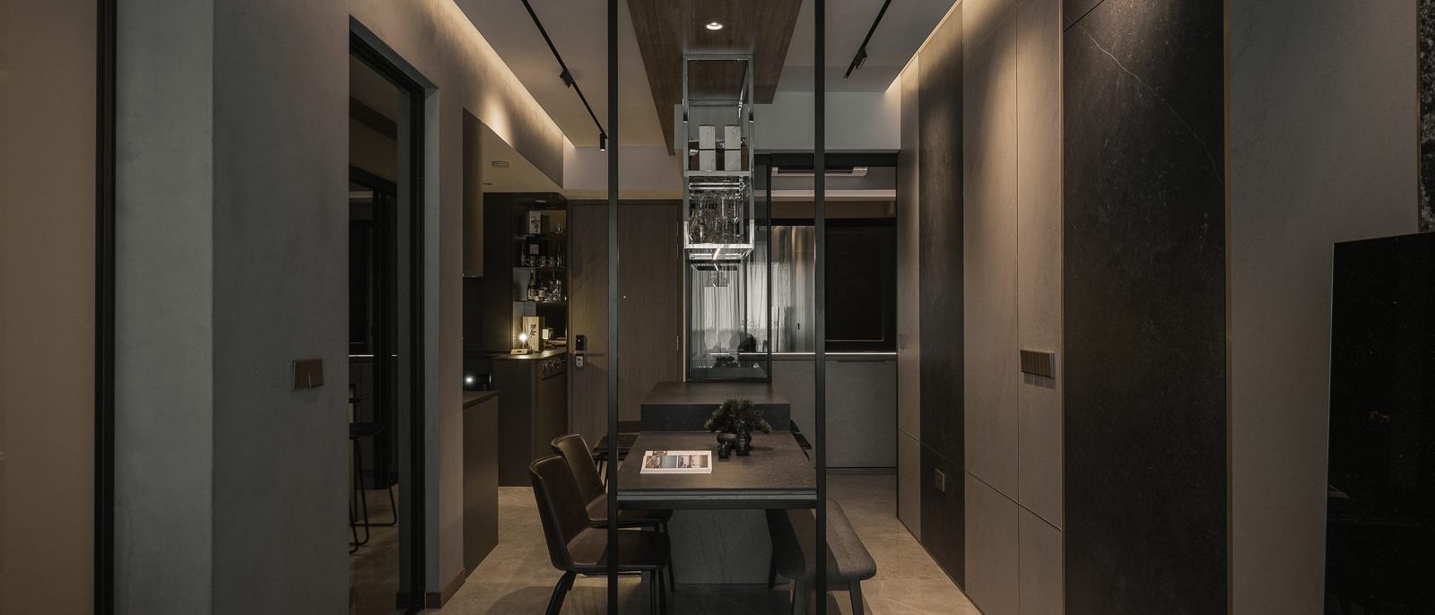 A suspended glass-and-steel wine rack anchors the dining area, framed by dark stone-clad walls and warm cove lighting.