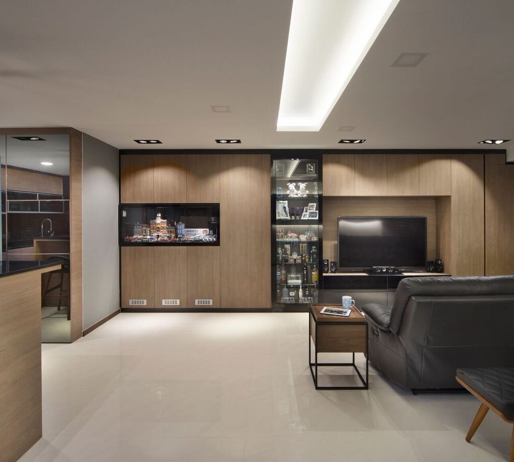 A tall glass-fronted display cabinet sits beside the TV wall, holding collectibles and spirits, with the dining table and cage pendants visible beyond