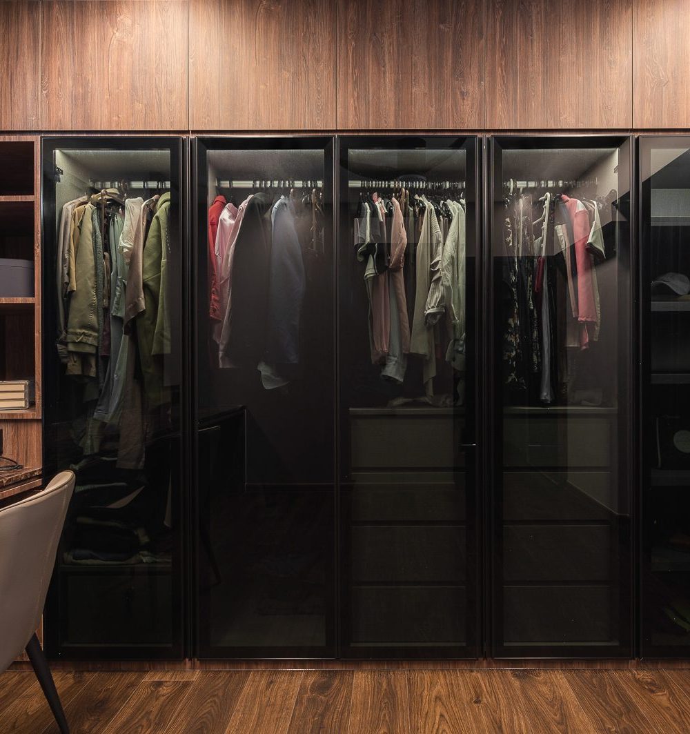 Smoked glass wardrobe doors run the full width of the dressing room, keeping clothing visible yet contained.