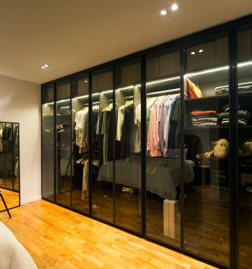 Backlit open shelving and hanging rails sit behind smoked glass doors, keeping the wardrobe's contents visible while staying tidy.