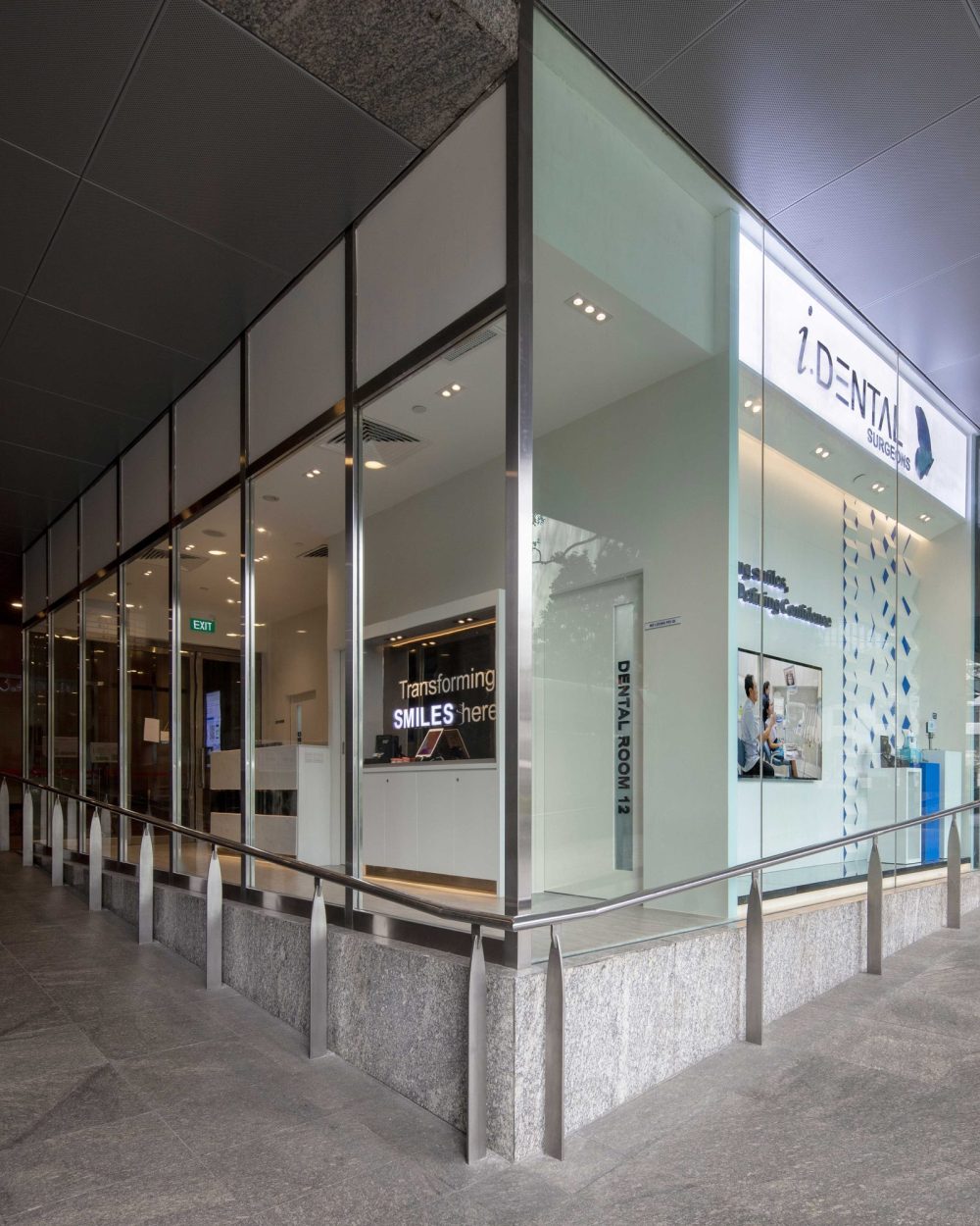 Full-height glazing wraps the clinic's corner unit, with illuminated signage visible from the walkway outside.
