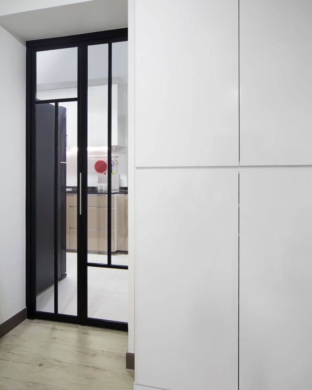 A black-framed glass sliding door marks the kitchen's entrance, letting light pass through while keeping cooking smells contained.