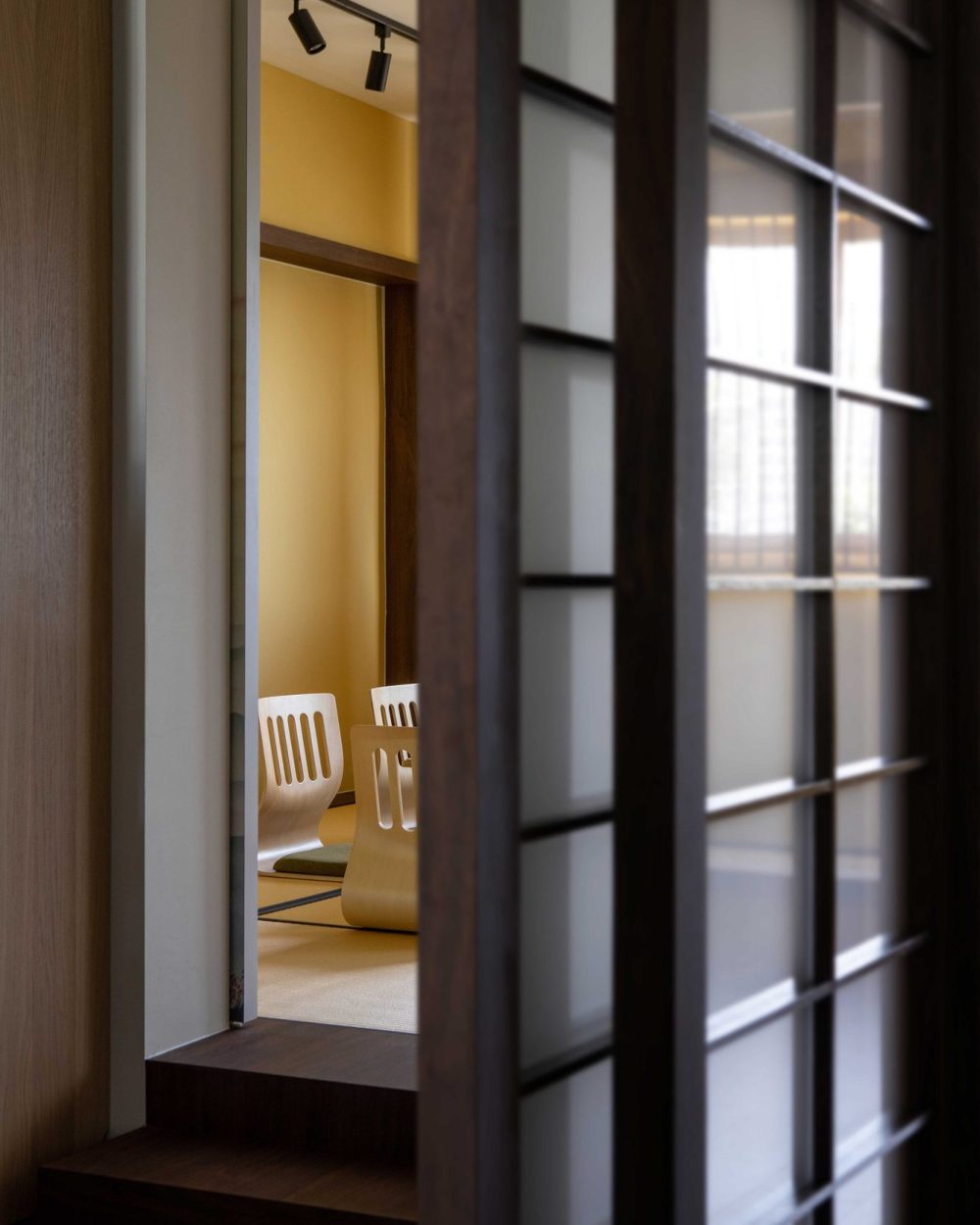 Chairs and tatami flooring are framed through a half-open shoji door, inviting a peek into the tea room beyond.
