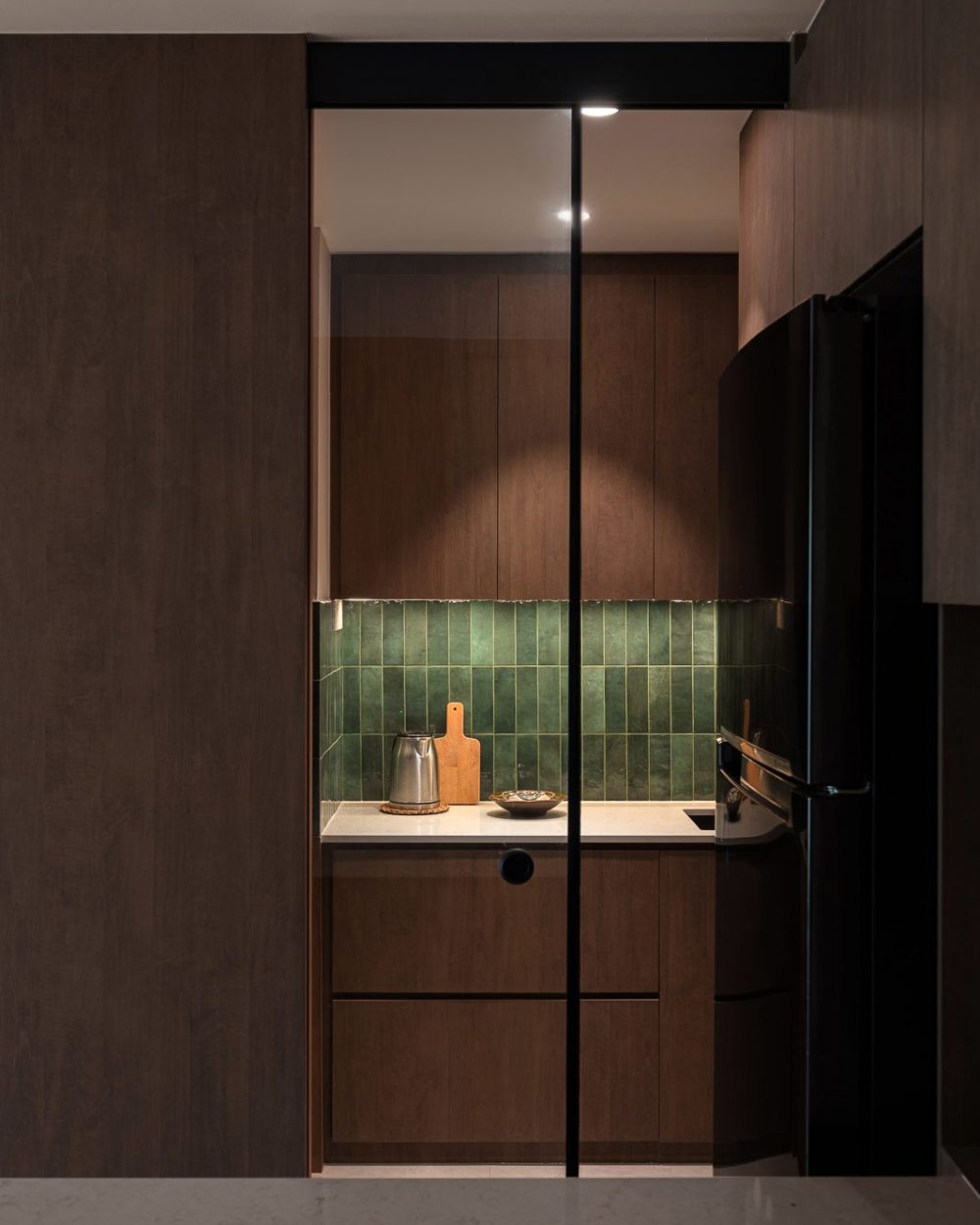 Handmade glossy green tiles line the wet kitchen's backsplash, paired with a stone counter and warm under-cabinet lighting.