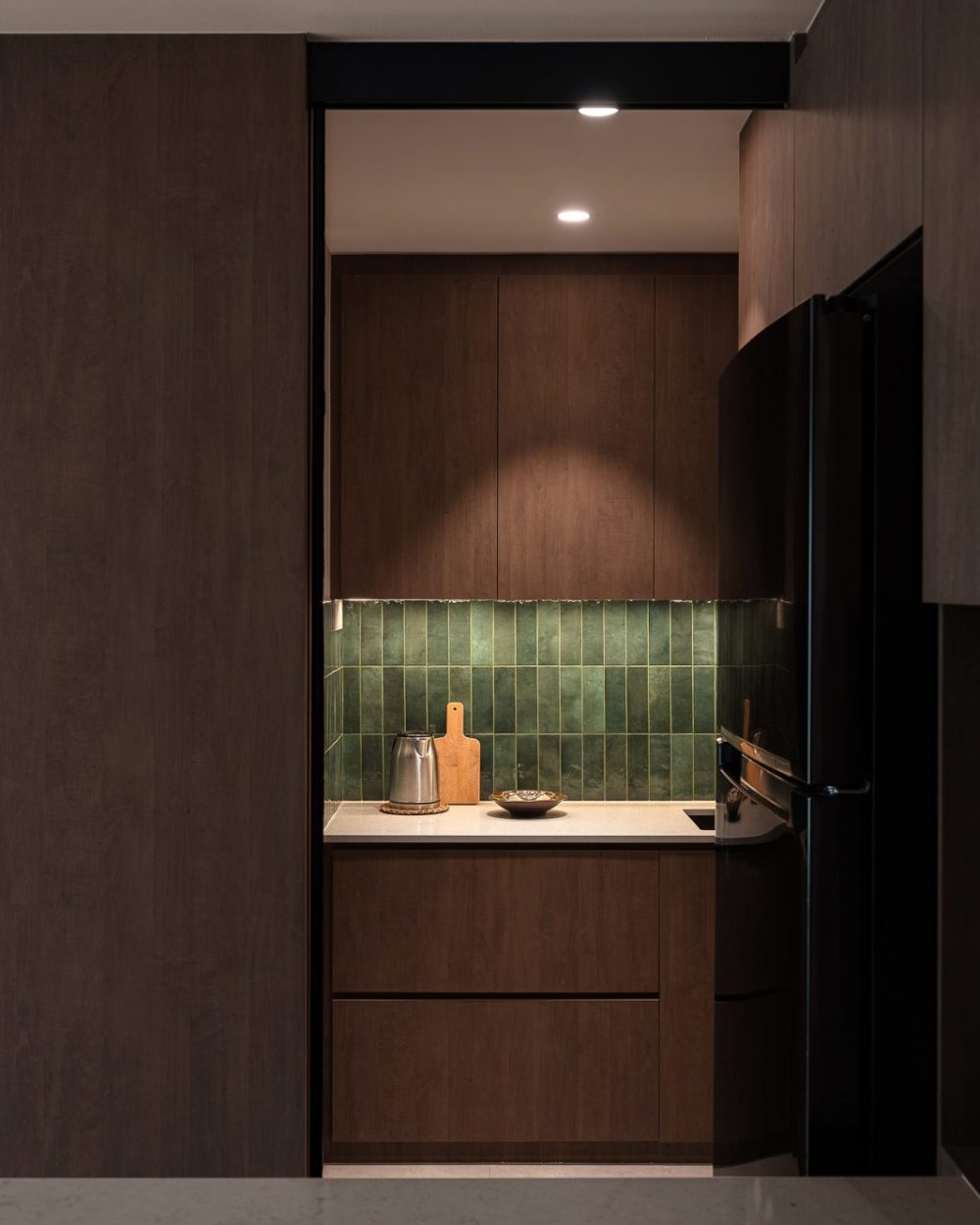 A sliding glass door reveals a glazed green tile wet kitchen, fitted with dark timber cabinetry and a built-in fridge.