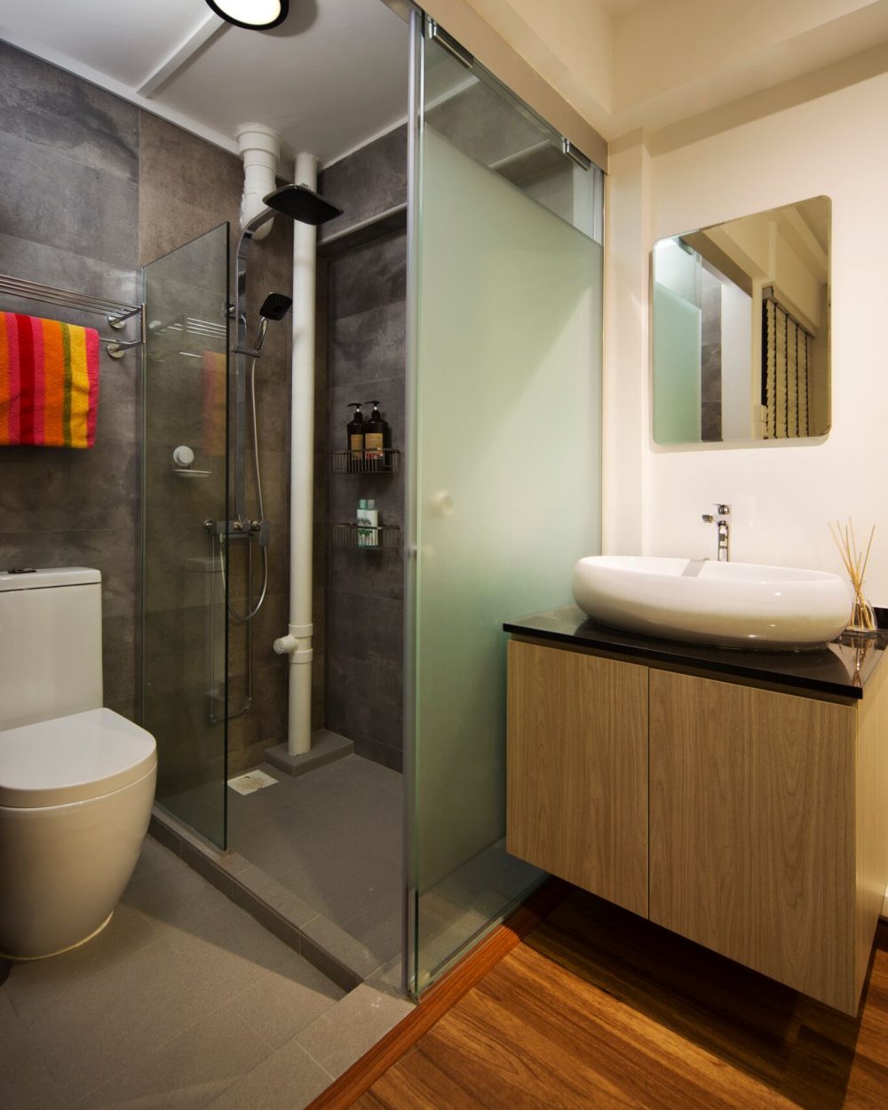 Large-format grey stone tiles line the shower and walls, paired with a floating wood vanity, black stone counter and a vessel sink.