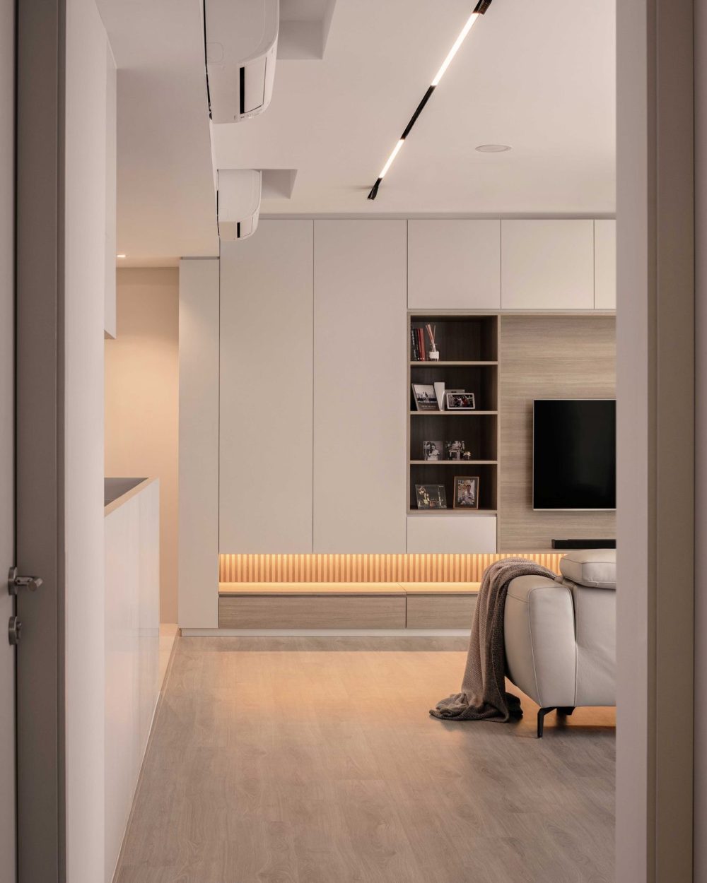 A slim black ceiling light line draws the eye down the hallway toward the living room's TV wall and bookshelf niche.