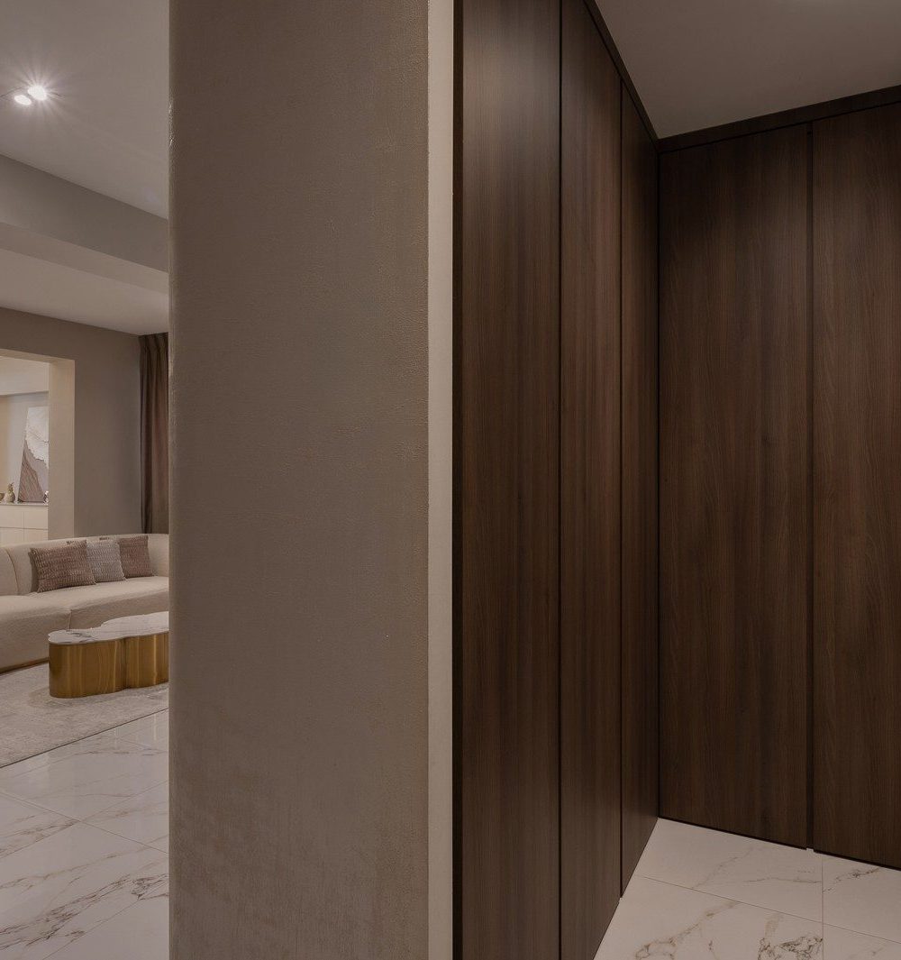 Full-height timber wardrobe doors line the entrance hallway, opening onto a view of the curved sofa and chandelier-lit dining area beyond.